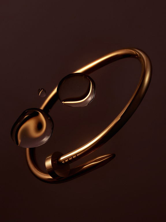 Close-up studio shot of an gold metal nail bracelet with water droplets, set against a dark brown background, highlighting luxury jewelry.