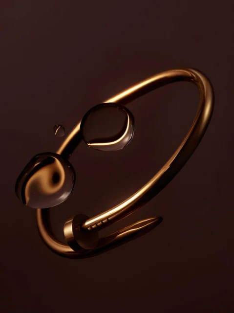 Close-up studio shot of an gold metal nail bracelet with water droplets, set against a dark brown background, highlighting luxury jewelry.