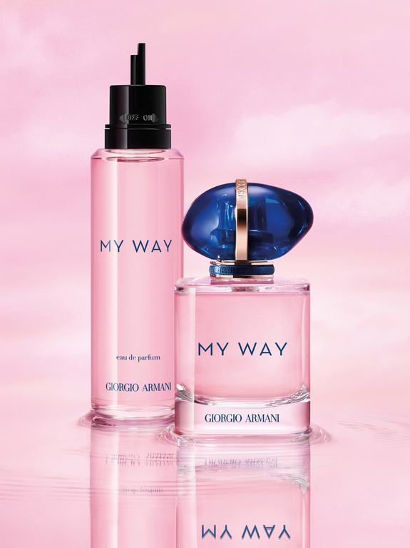 Two pink Giorgio Armani My Way perfume bottles stand on a reflective surface against a soft pink cloudscape background.