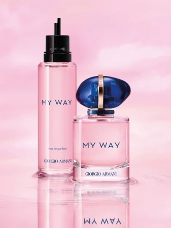 Two pink Giorgio Armani My Way perfume bottles stand on a reflective surface against a soft pink cloudscape background.
