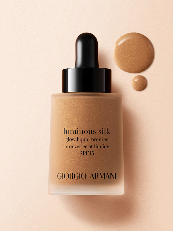 Giorgio Armani Luminous Silk glow liquid bronzer with black dropper, and bronzer droplets on a light peach background.