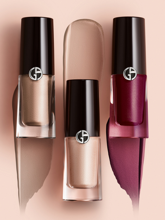 Three Giorgio Armani beauty products: clear bottles with black lids and liquid makeup swatches on a light pink background, close-up.