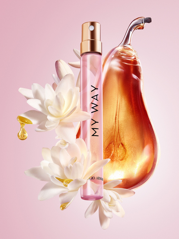 Still life of Giorgio Armani's 'My Way' perfume bottle surrounded by white flowers, golden liquid pear sculpture on light pink background.