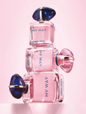 Three stacked Giorgio Armani My Way perfume bottles with pink liquid and dark blue gemstone caps on a pink background.