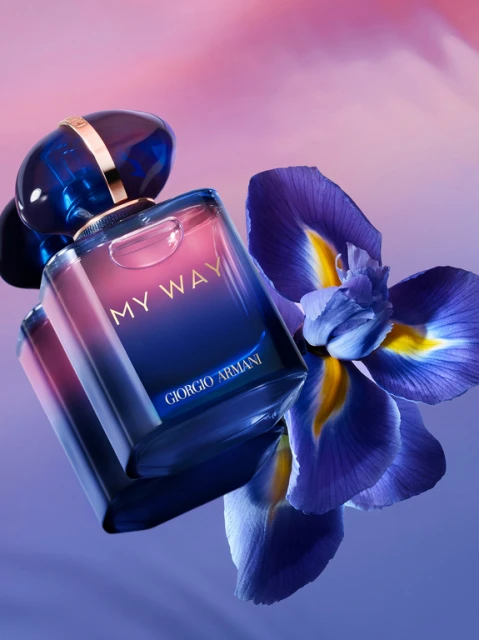 Giorgio Armani 'My Way' perfume bottle with purple iris flower against a gradient pink and blue background in a beauty shot.