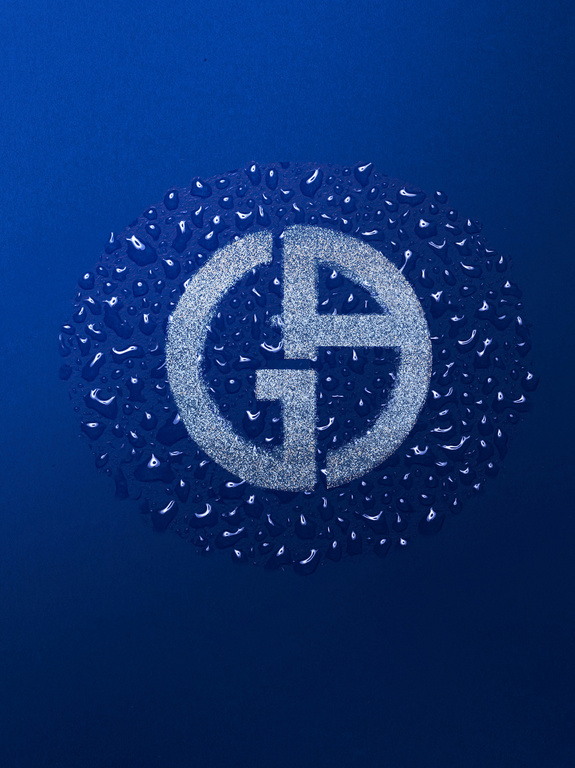 Close-up of the Giorgio Armani logo, encircled by water droplets against a blue background, creating a textured, shimmering effect.