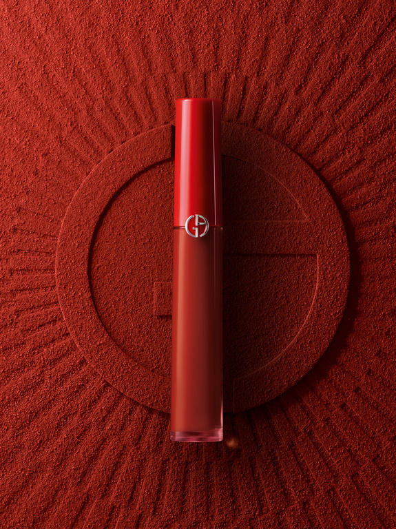 Close-up studio shot of Giorgio Armani red lipstick against a textured red background with an embossed G logo design.