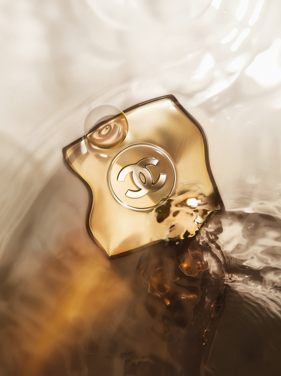 Close-up studio shot of Chanel fragrance bottle in water with blurred background. Golden hues dominate the artistic still life image.