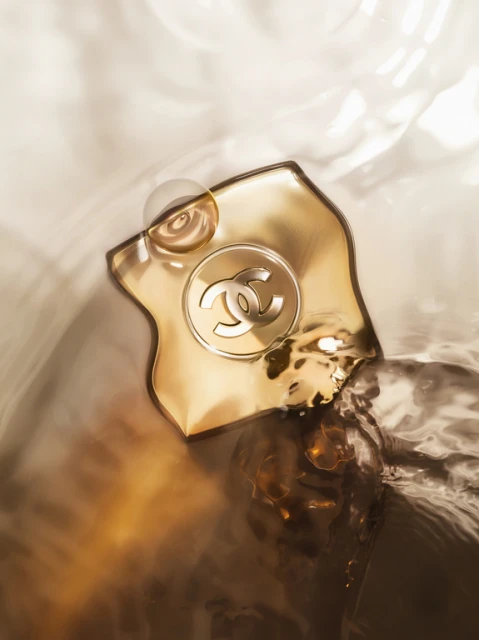 Close-up studio shot of Chanel fragrance bottle in water with blurred background. Golden hues dominate the artistic still life image.