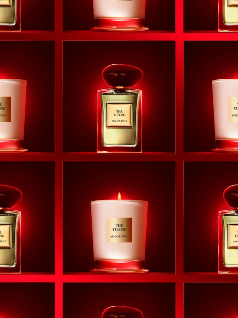 Aesthetic arrangement of The Yulong by Armani Prive perfume bottle and candle against a red shelf backdrop in an eye-level studio shot.