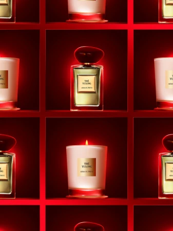 Aesthetic arrangement of The Yulong by Armani Prive perfume bottle and candle against a red shelf backdrop in an eye-level studio shot.
