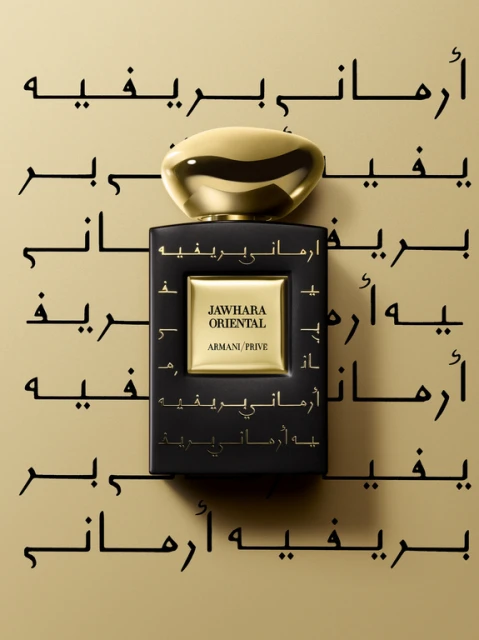 Close-up studio shot of a black Armani Prive fragrance bottle with a gold cap, featuring Arabic text and minimal lighting. 