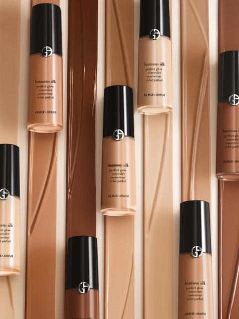 Giorgio Armani Luminous Silk Perfect Glow concealer bottles in various shades arranged on matching colored glossy fluid background.