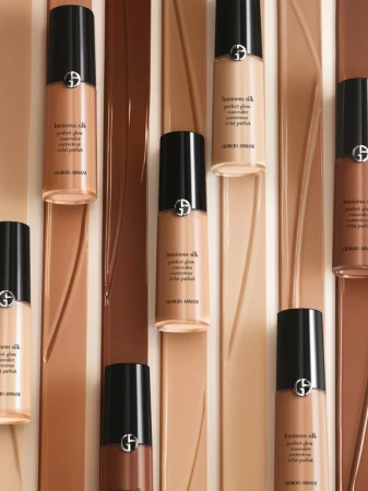 Giorgio Armani Luminous Silk Perfect Glow concealer bottles in various shades arranged on matching colored glossy fluid background.