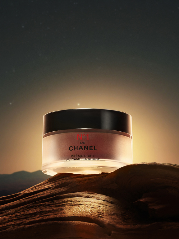 Chanel No. 1 de Chanel cream jar on a textured brown surface set against a dark sky with light glows, in a product still life.