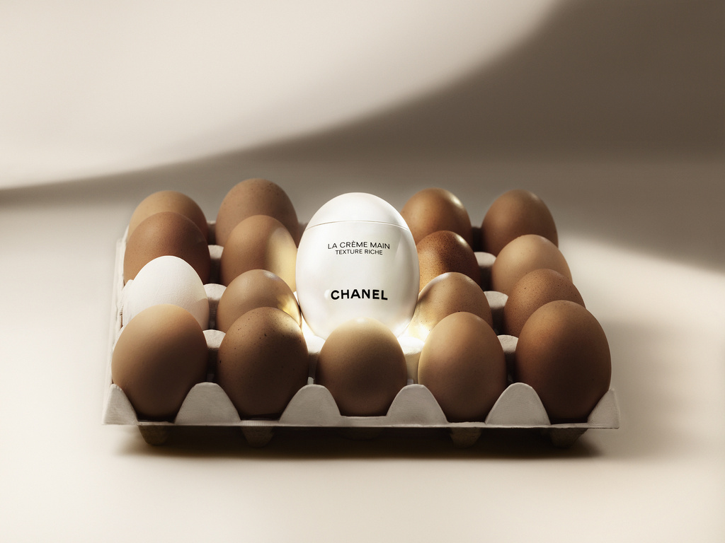Cosmetic product placed within an egg carton, surrounded by brown and one white egg against a pale, illuminated backdrop.