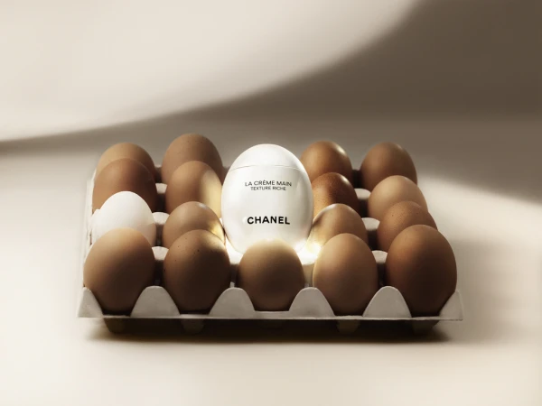 Cosmetic product placed within an egg carton, surrounded by brown and one white egg against a pale, illuminated backdrop.
