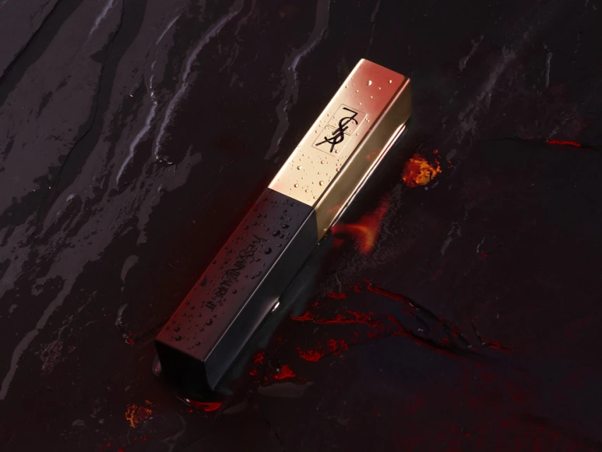 YSL lipstick tube in gold and black on wet slate background, highlighting luxury beauty product with logo and reflective surface.