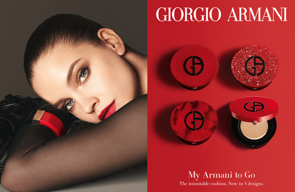 Advertisement for Giorgio Armani makeup features a model with red lipstick and four red Armani cushion compacts against a red background.