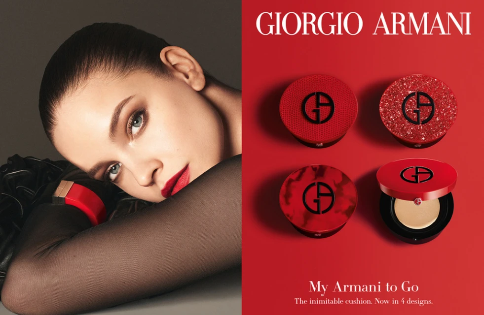 Advertisement for Giorgio Armani makeup features a model with red lipstick and four red Armani cushion compacts against a red background.