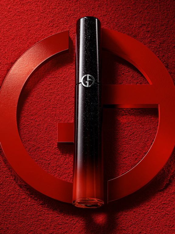 Close-up studio shot of Giorgio Armani lipstick with signature logo against textured red backdrop with graphic brand elements.