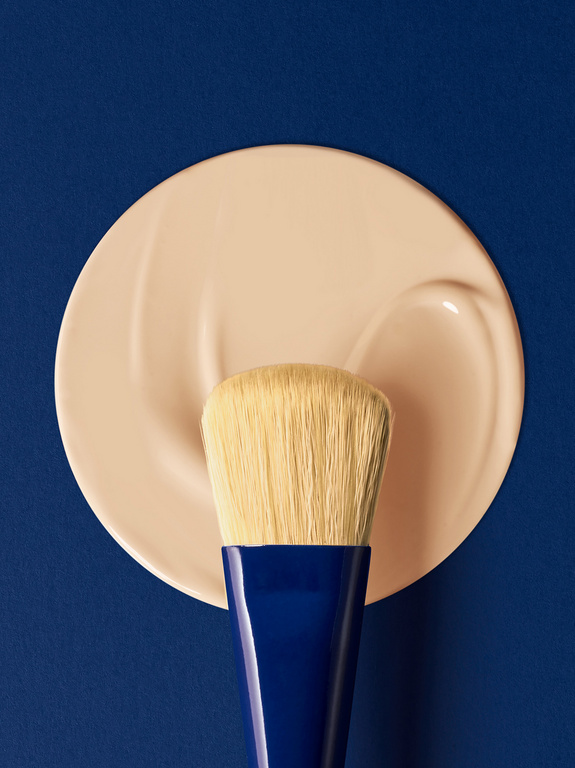Close-up studio shot of a makeup brush resting on a beige foundation smear against a dark blue background, cosmetics and beauty concept.