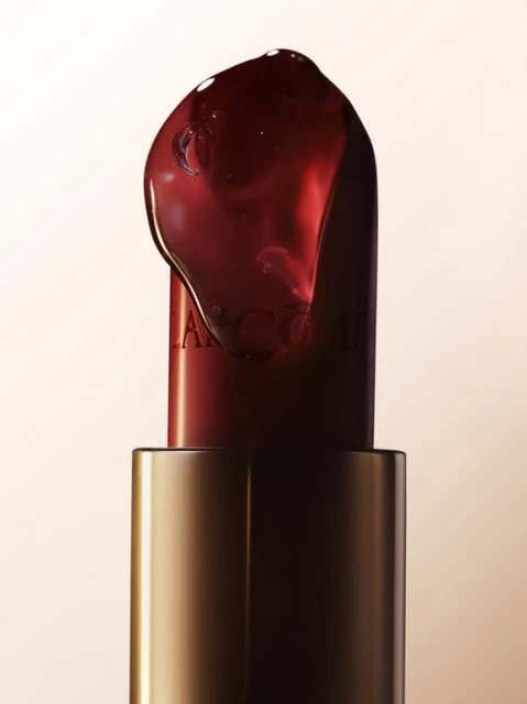 Close-up of a red lipstick tube with gel, highlighting a luxurious beauty product in a studio setting against a soft beige background.