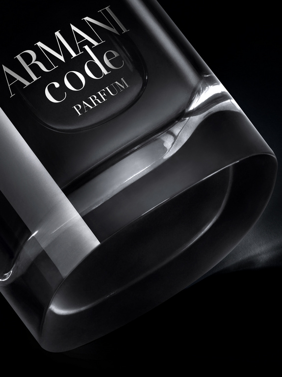 Close-up of a black Armani Code Parfum bottle against a dark background with a clear, angular design and white text on the bottle.
