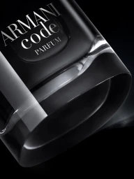 Close-up of a black glass Armani Code Parfum bottle angled against a dark background with bright specular highlights.