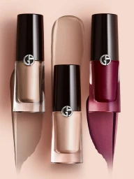 Three cosmetic bottles with metallic caps and swatches of liquid makeup on a pale background