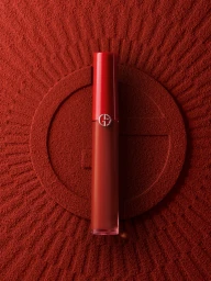 Red cosmetic product tube resting vertically on a textured red powder background with a stamped circular logo