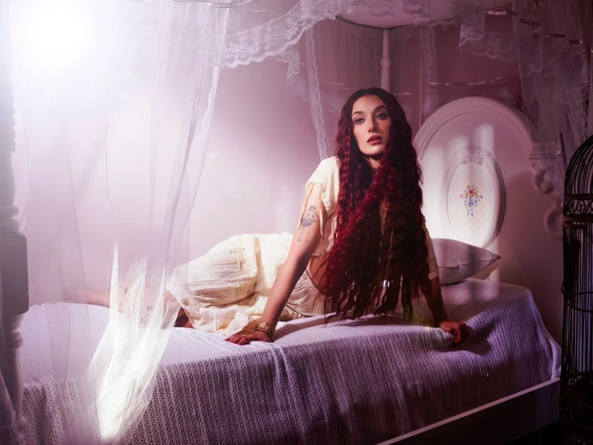 Portrait of a woman with long red hair laying on a bed. Soft, diffused lighting enhances the scene, creating a serene, intimate mood.