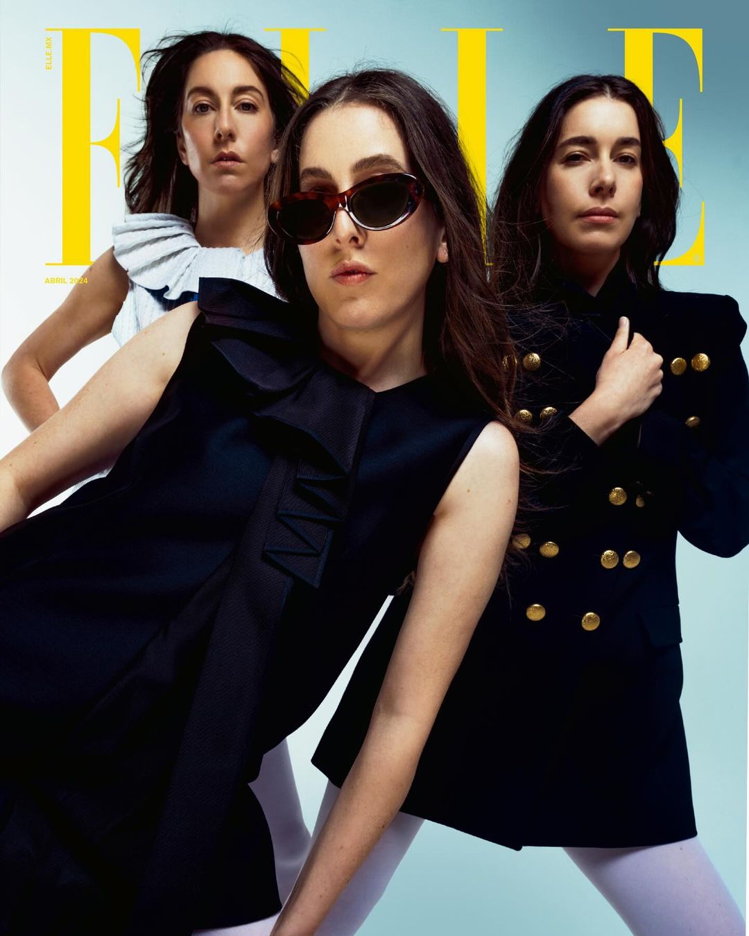 Three women on the cover of Elle magazine in a studio shot. Two wear black tops with white tights; one wears sunglasses.