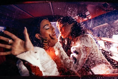 Two women intimately posed inside a car interior covered in water droplets with dramatic red and purple lighting by Callum Walker Hutchinson
