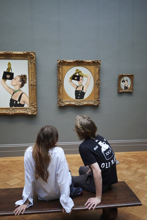 Two people sitting on a bench, viewing framed illustrations in an art gallery with light hardwood floors and soft lighting.