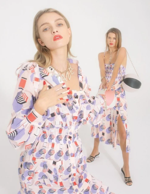 Two fair-skinned women pose in patterned mini dresses and sandals against a bright white backdrop in a fashion-forward editorial shot.