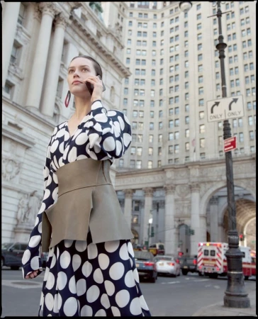 Woman in polka dot dress uses her cell phone in an urban environment. Buildings, traffic and ambulance are visible in the background.