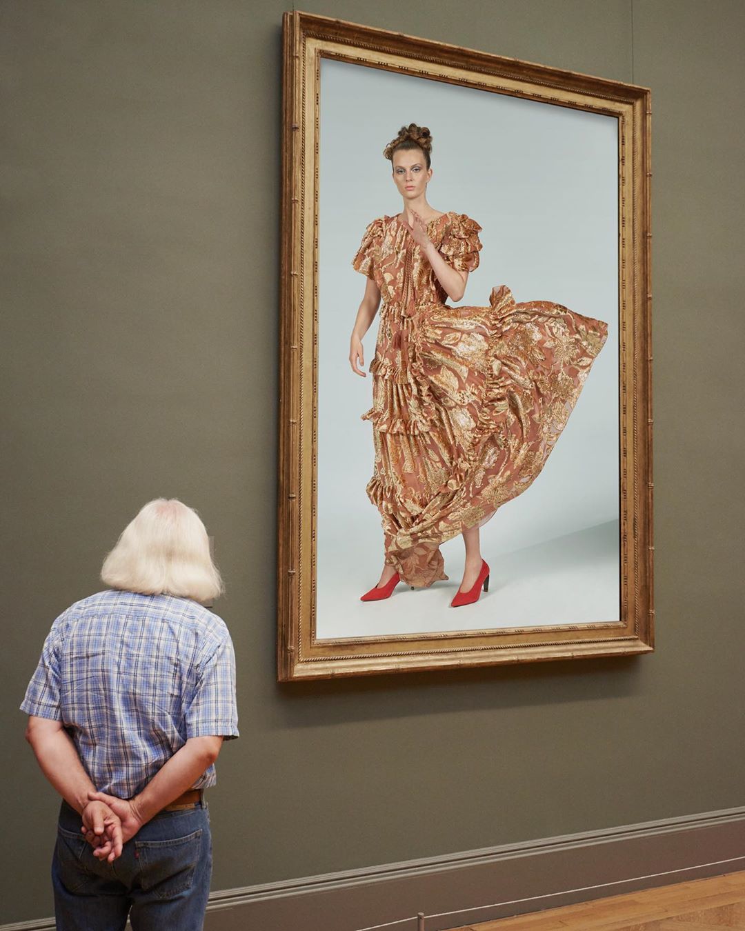 Person views a painting of a woman wearing a gold gown and red shoes, displayed in a gold frame in a museum or art gallery.