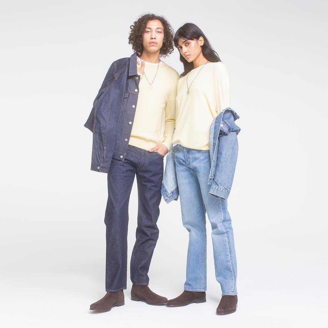 Two fashion models pose in matching jeans and yellow sweaters in a studio with soft, diffused lighting, casting minimal shadows.