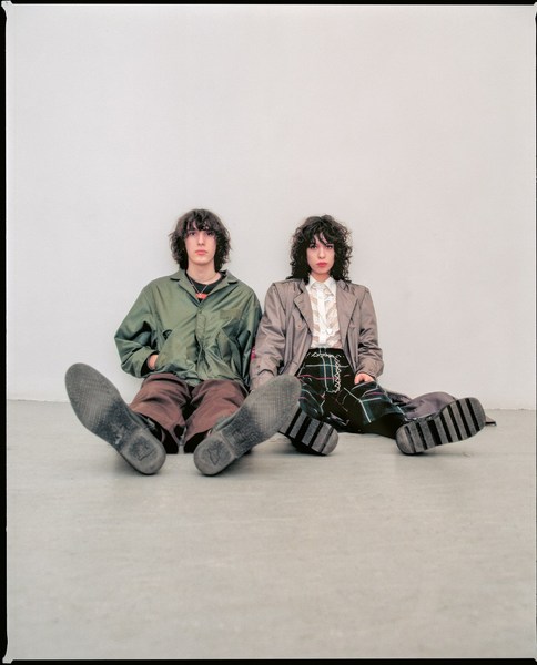 Two models sitting on a grey floor against a light wall, photographed by Cesar Love Alexandre.