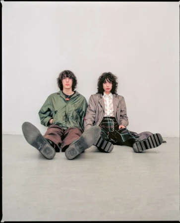 Two models sitting on a grey floor against a light wall, photographed by Cesar Love Alexandre.