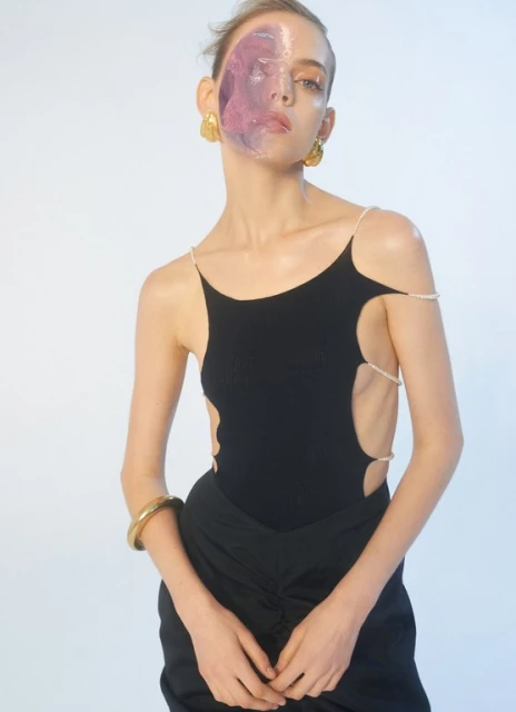 A striking studio shot of a woman wearing a black top and skirt, adorned with pearl straps, enhanced by a vibrant purple facial overlay.
