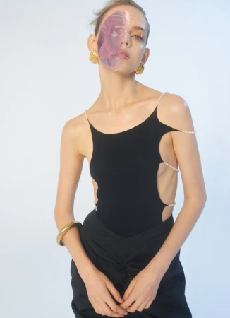 A striking studio shot of a woman wearing a black top and skirt, adorned with pearl straps, enhanced by a vibrant purple facial overlay.