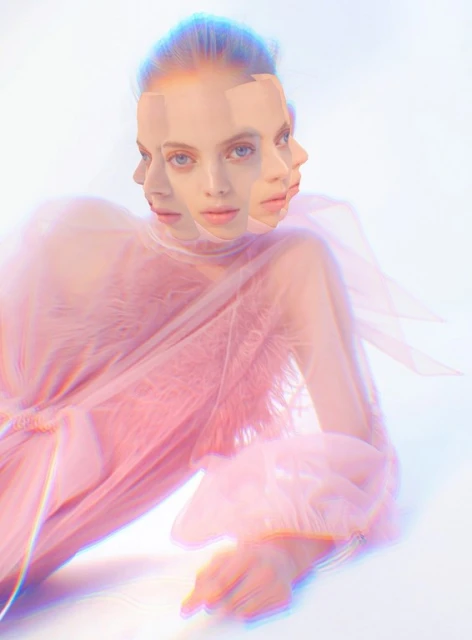 Woman with multiple face exposures in a layered collage wearing a light pink gown, lying down in a bright white indoor setting.