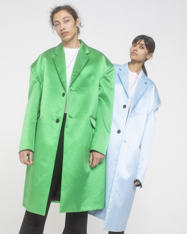 Two models standing against a white seamless background wearing oversized satin coats in bright green and light blue.