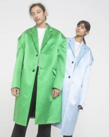 Two models standing against a white seamless background wearing oversized satin coats in bright green and light blue.