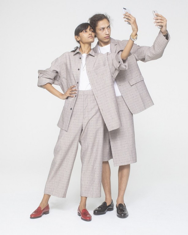 Two fashion models in matching plaid outfits posing in a photo studio while taking a selfie with a smartphone against a white backdrop.