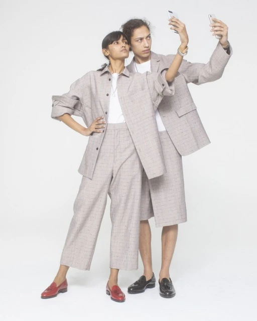 Two fashion models in matching plaid outfits posing in a photo studio while taking a selfie with a smartphone against a white backdrop.