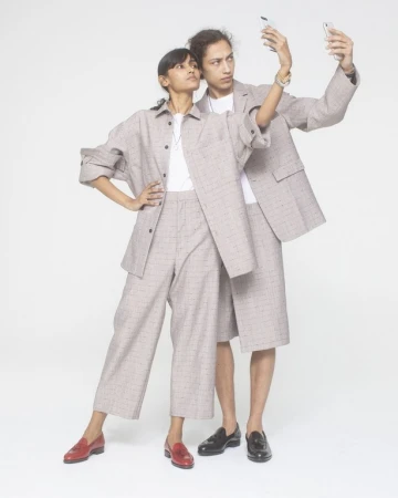 Two fashion models in matching plaid outfits posing in a photo studio while taking a selfie with a smartphone against a white backdrop.