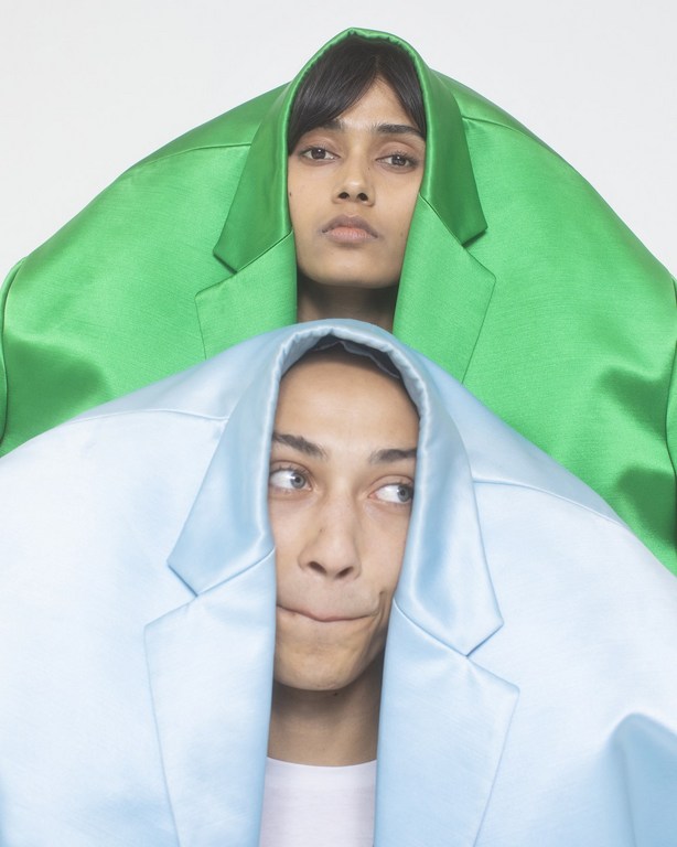 Two models posing with brightly colored blazers pulled over their heads against a plain white background by Cesar Love Alexandre.